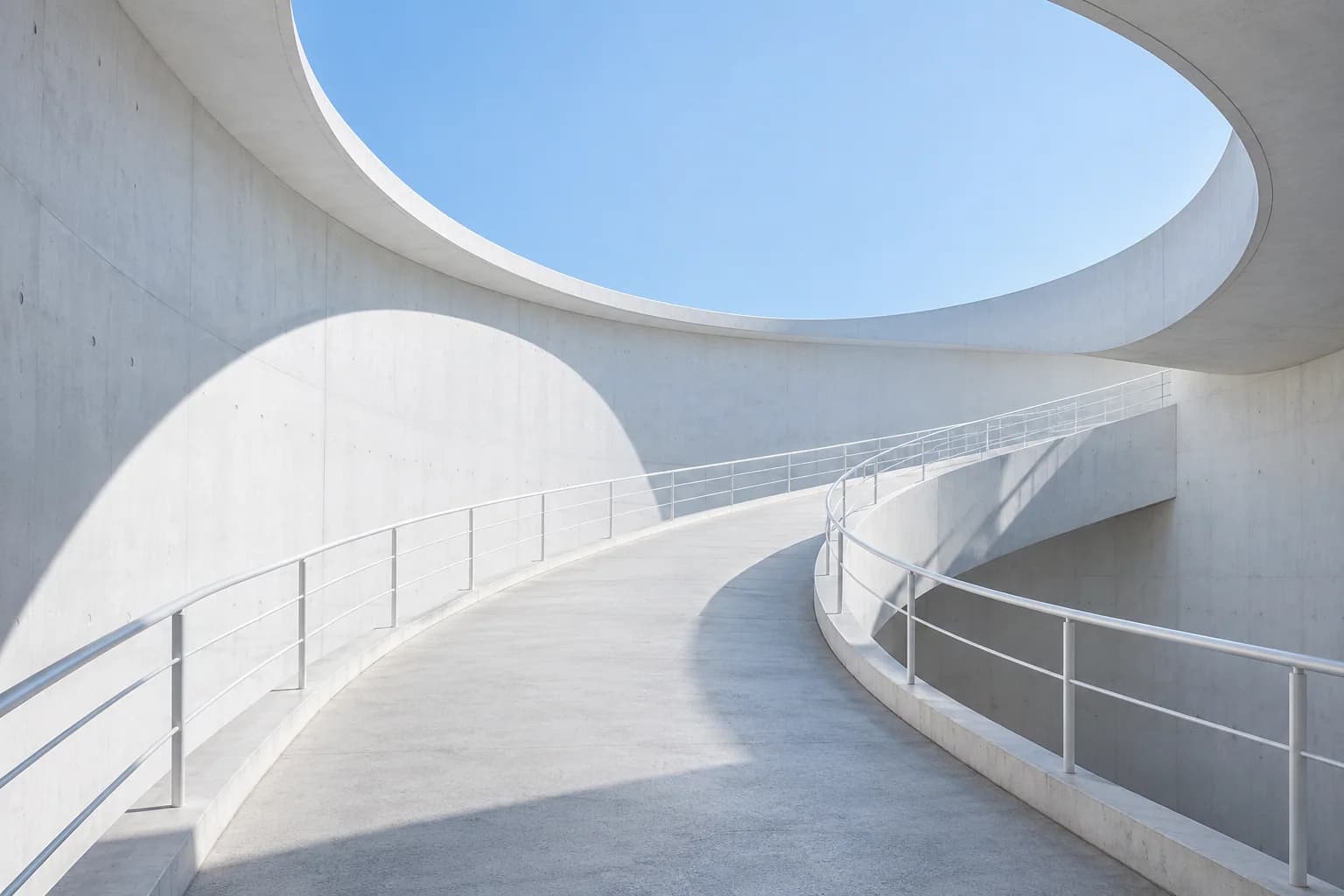 A curved white architectural pathway under an open blue sky